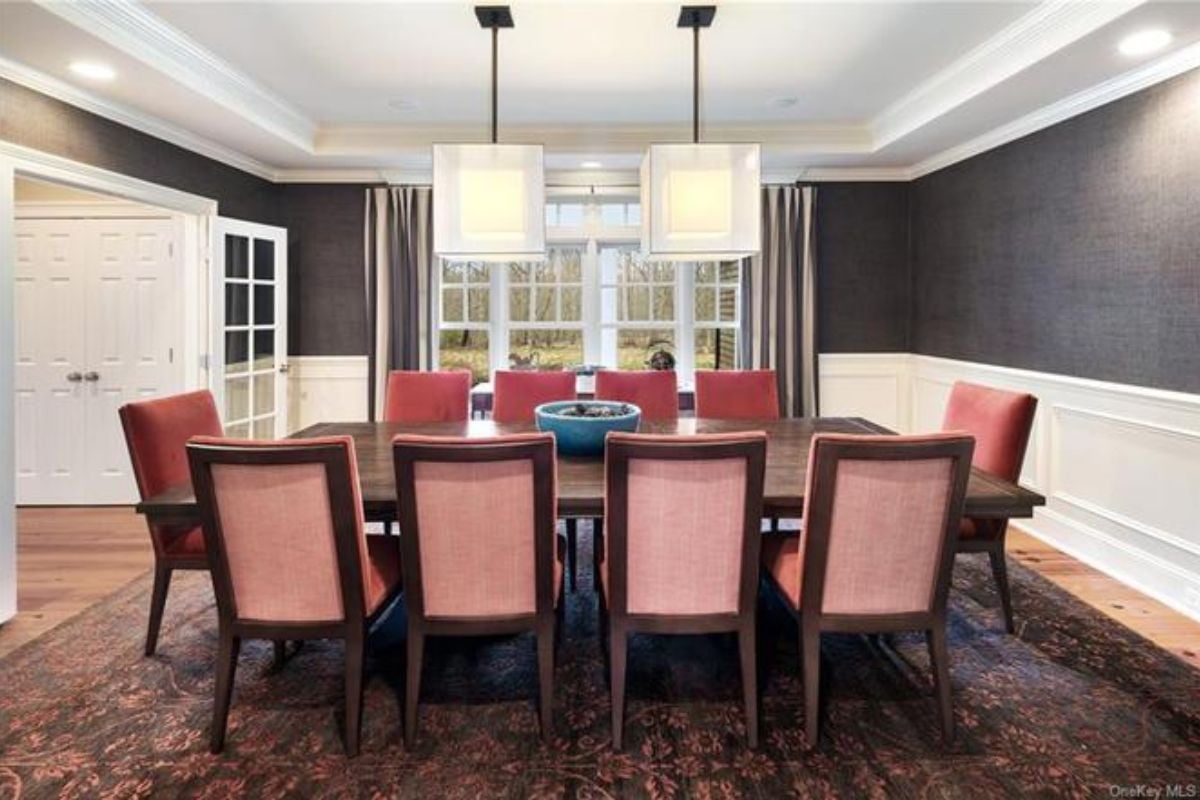 A dining room with windows, a rug, and a dining table surrounded by chairs.