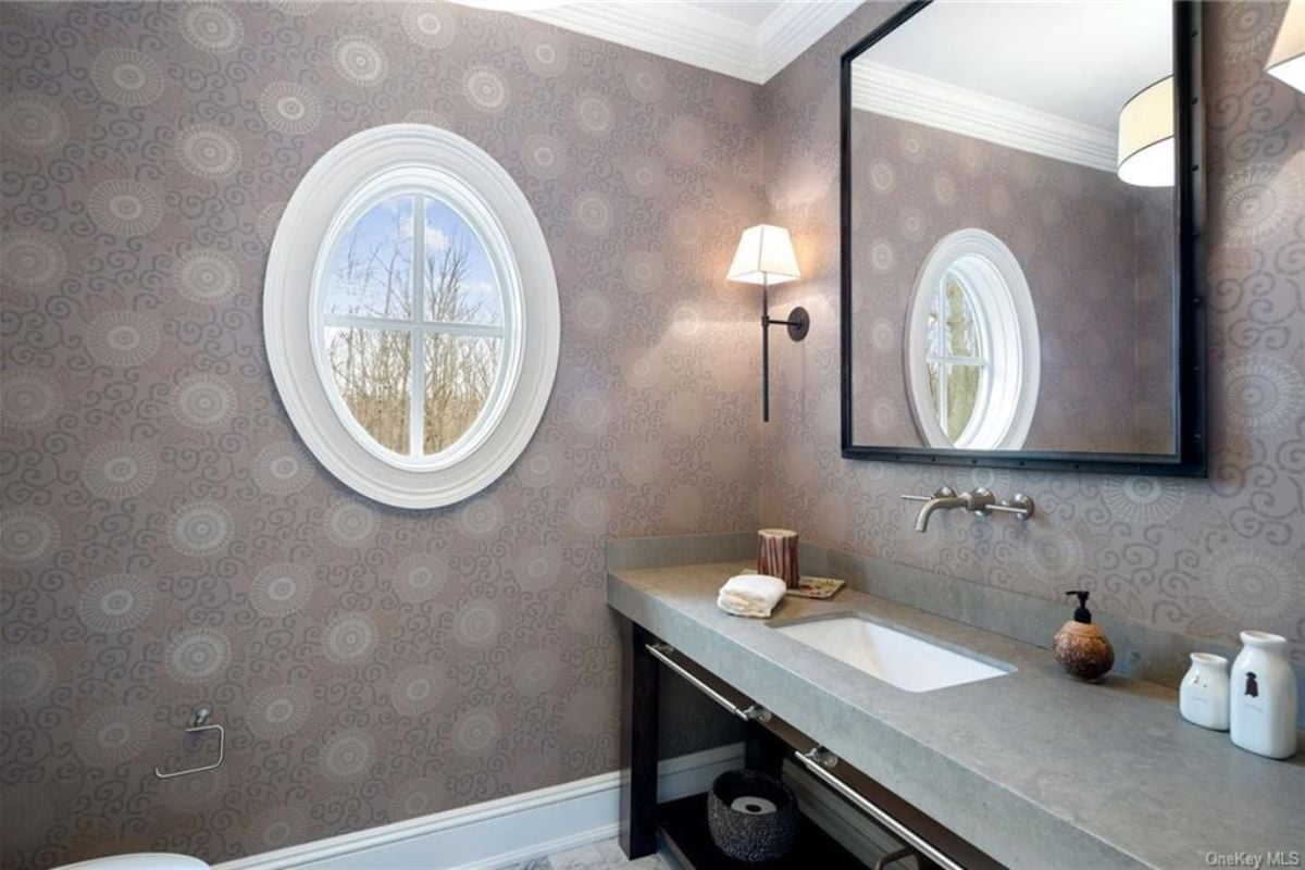 A bathroom with wallpaper, a window, countertop, and sink.