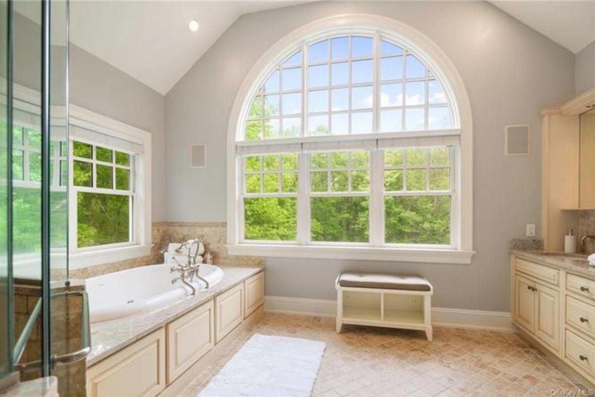 A bathroom with tiled floors, windows, cabinets, and a bathtub.