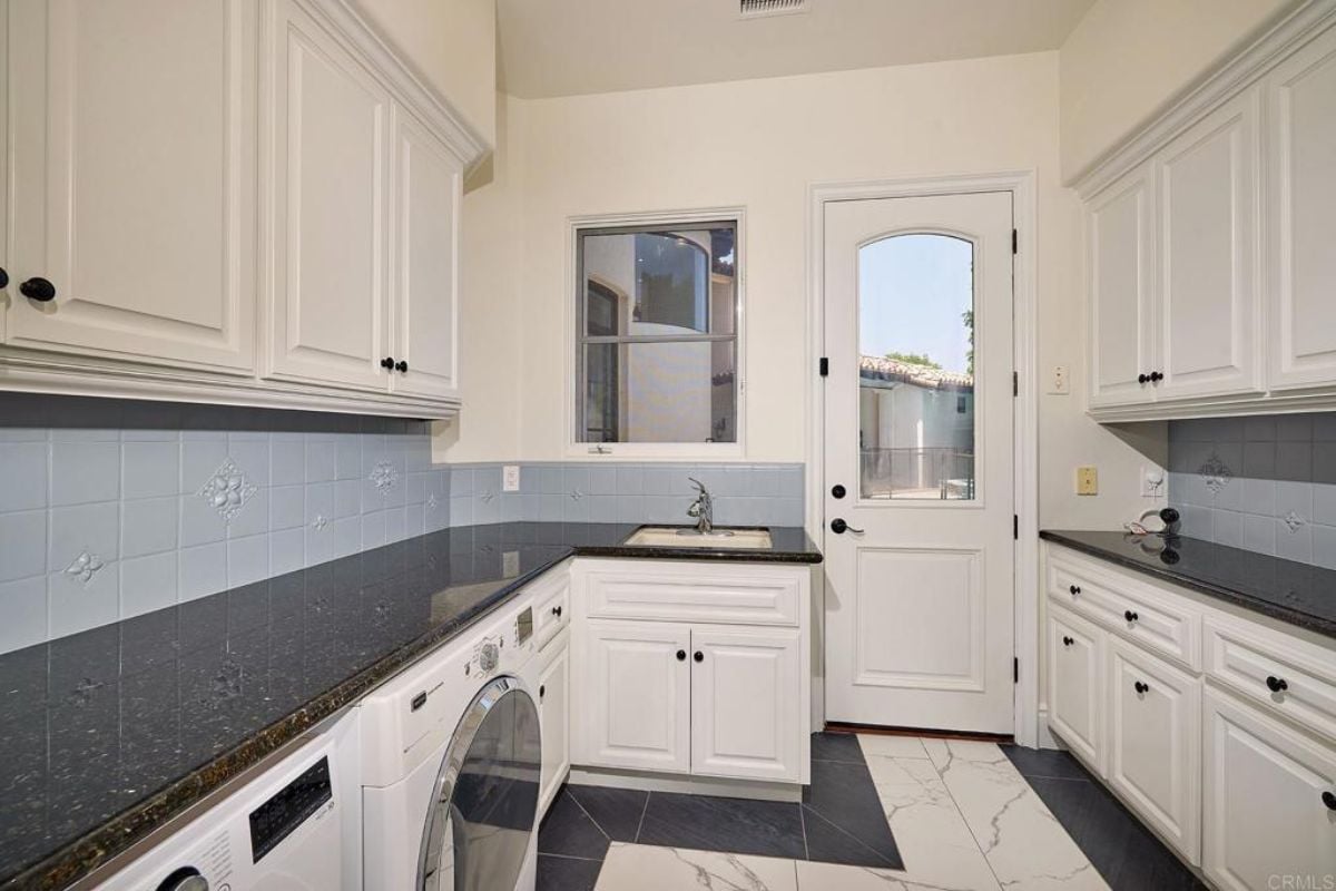A laundry room with countertops, sink, cabinets, and washing machine.