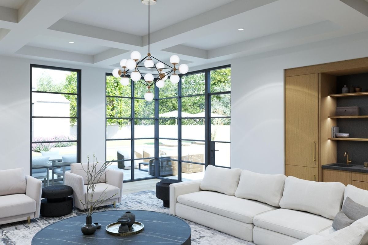 A dining room with a chandelier, exposed beam ceiling, windows, cabinets, white couches, and a round center table.