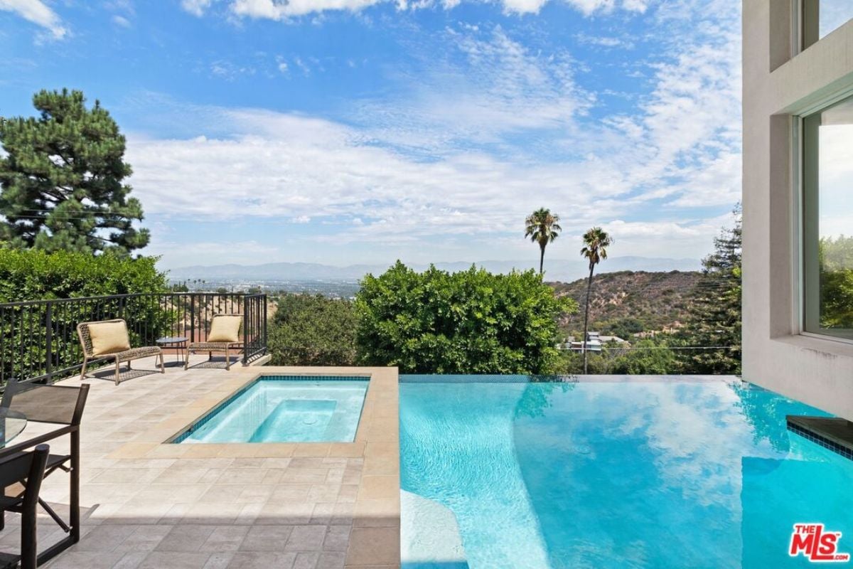 A swimming pool with a jacuzzi and chairs on the poolside.
