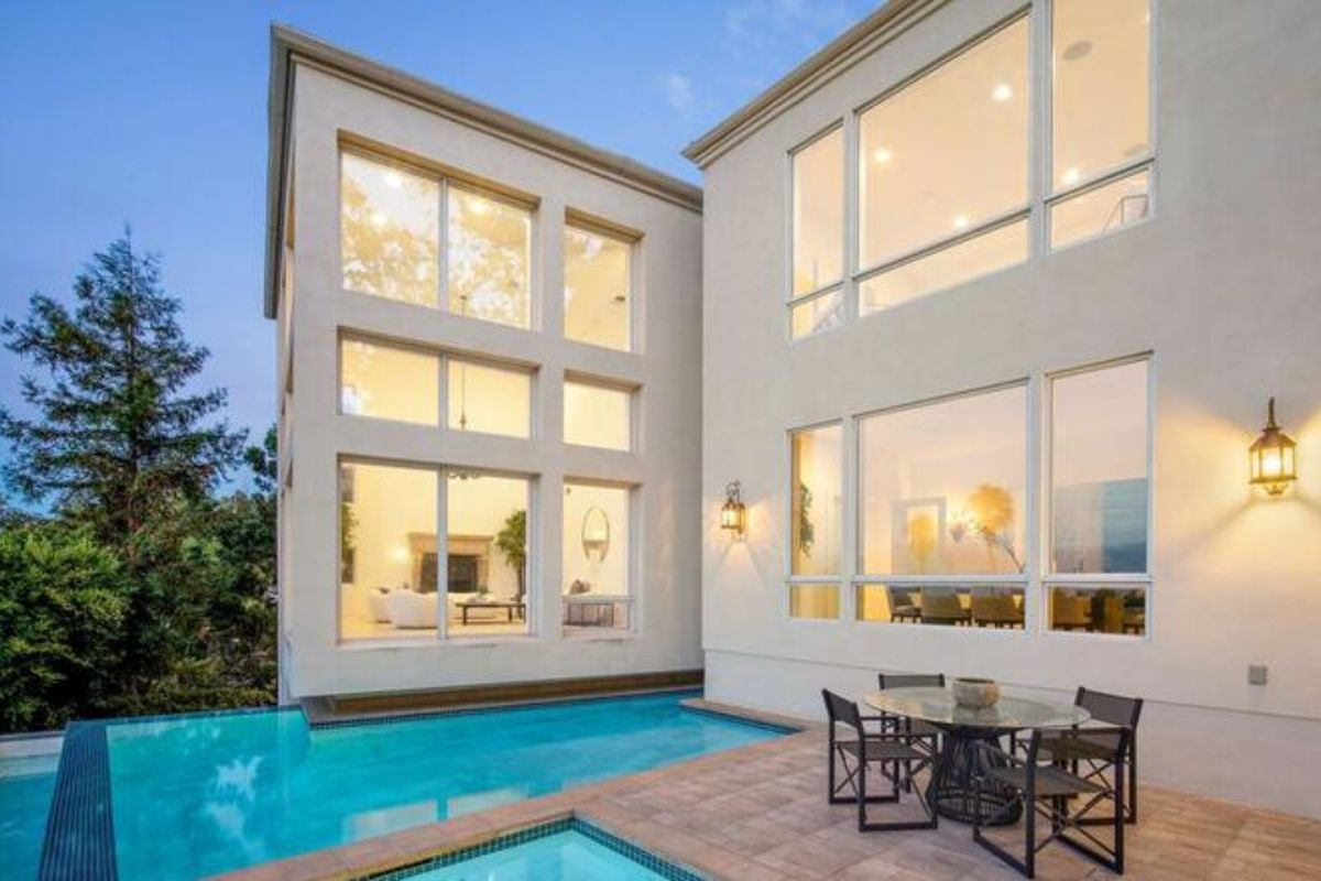 A swimming pool with a jacuzzi and table surrounded by chairs on the poolside.