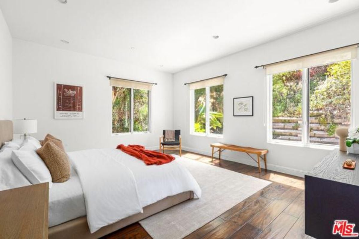 A bedroom with a bed, windows, a chair, and a bench.