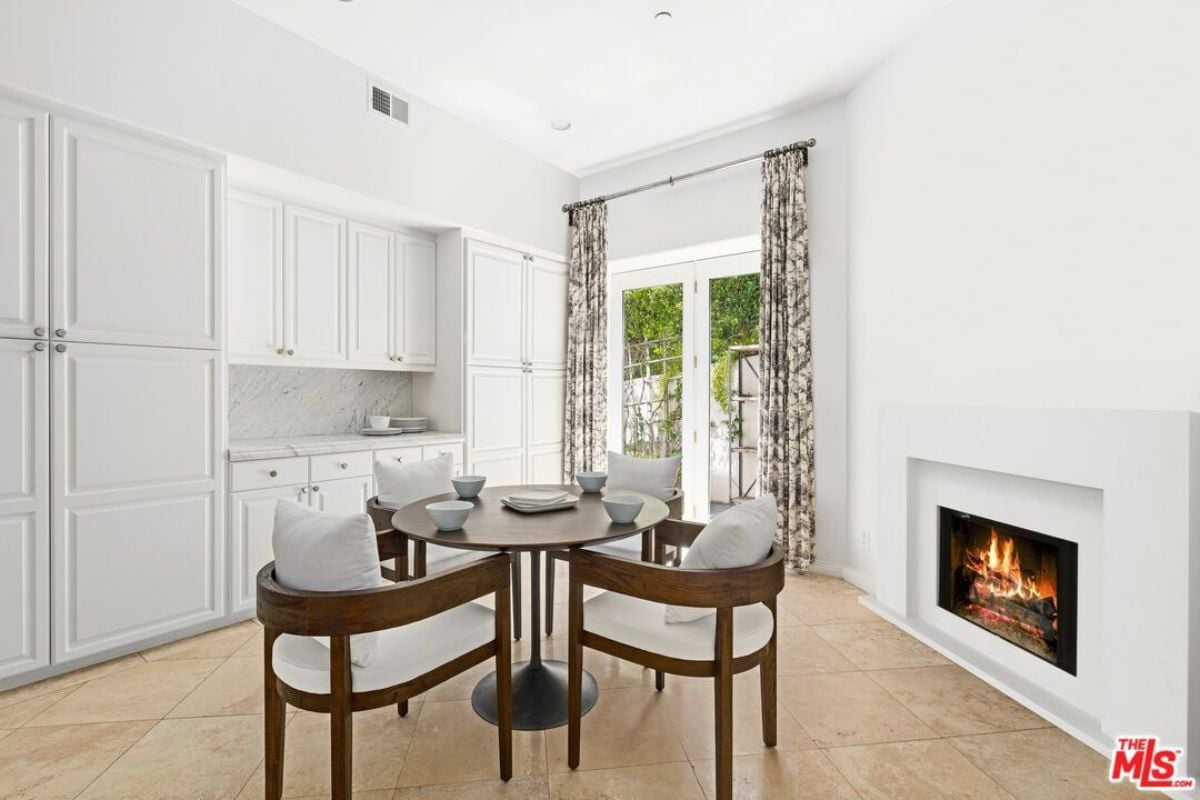 A breakfast nook with a fireplace, window, cabinets, and a coffee table surrounded by chairs.