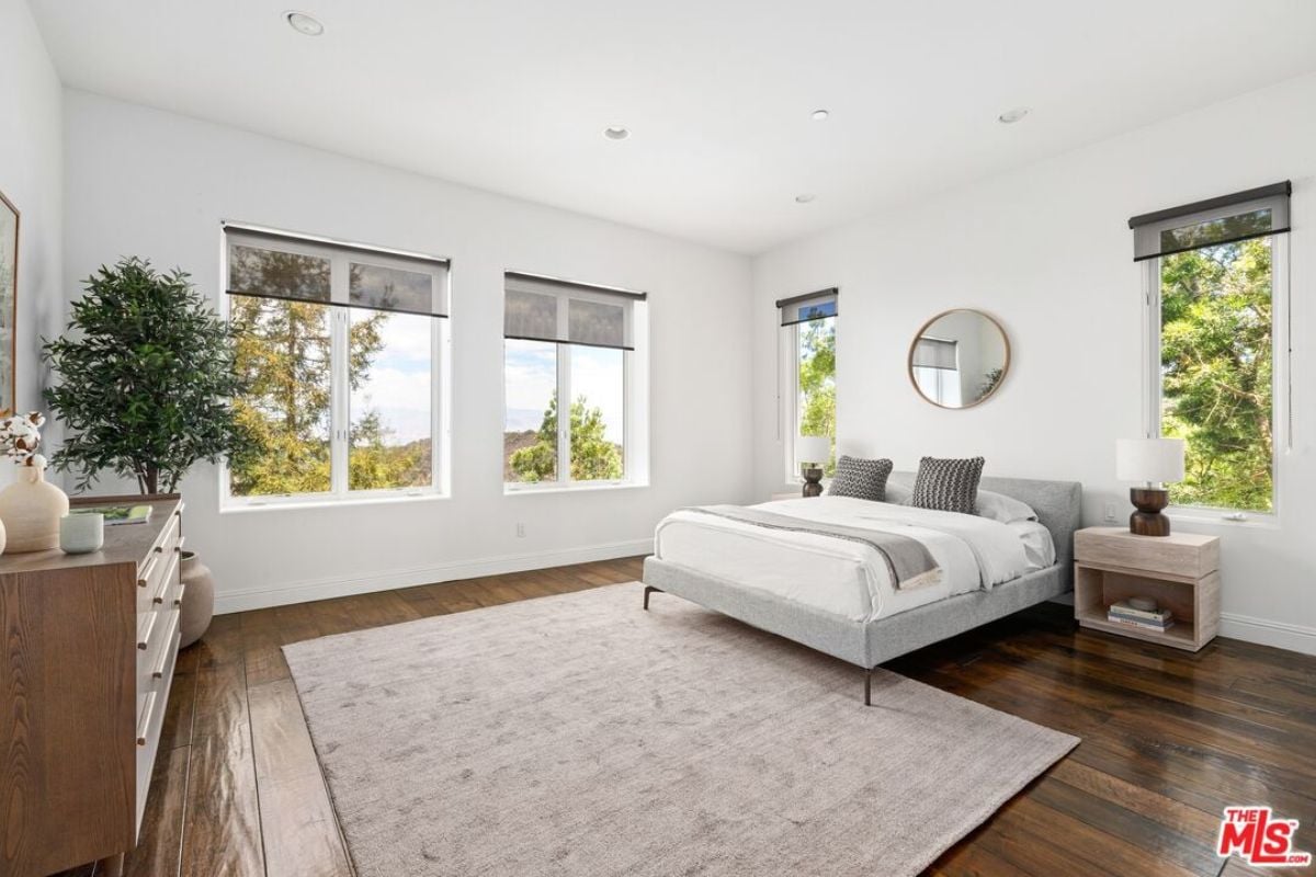 A bedroom with a bed, potted plant, windows, nightstand, and a cabinet.