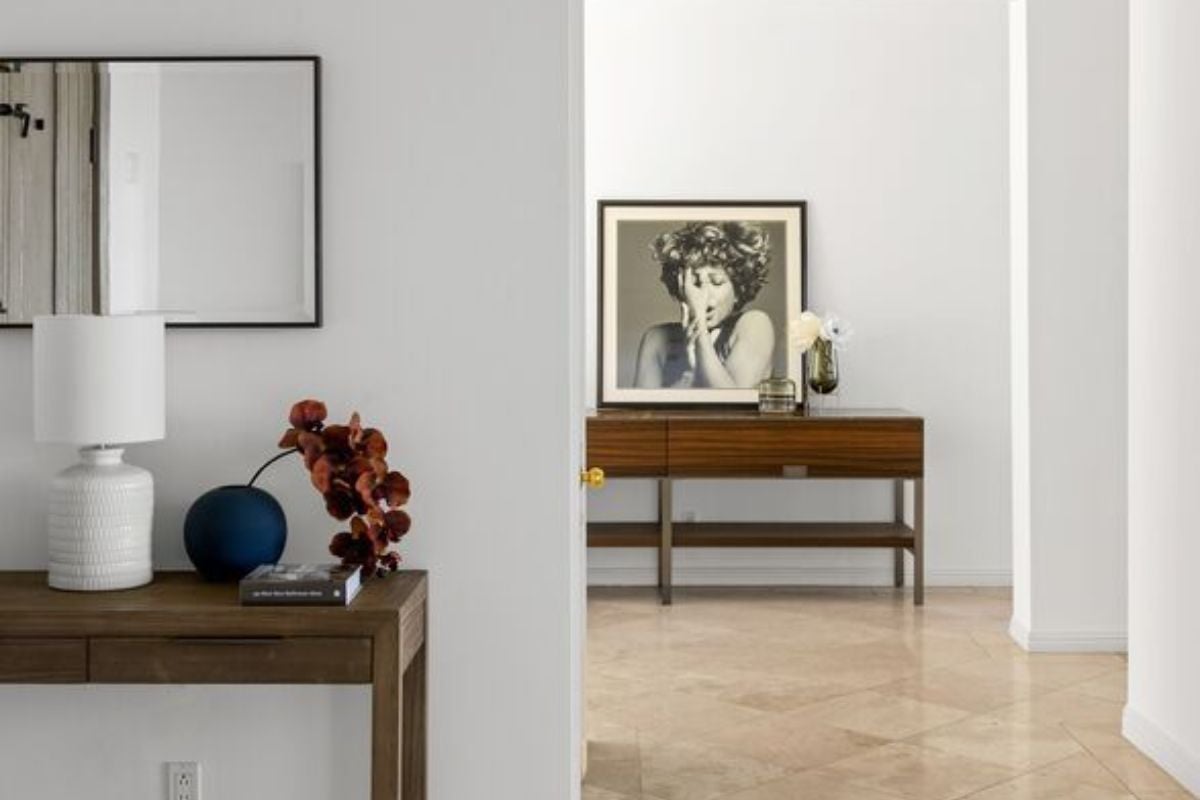 A foyer with a tiled floor, mirror, and a table adorned with a lamp and vase.