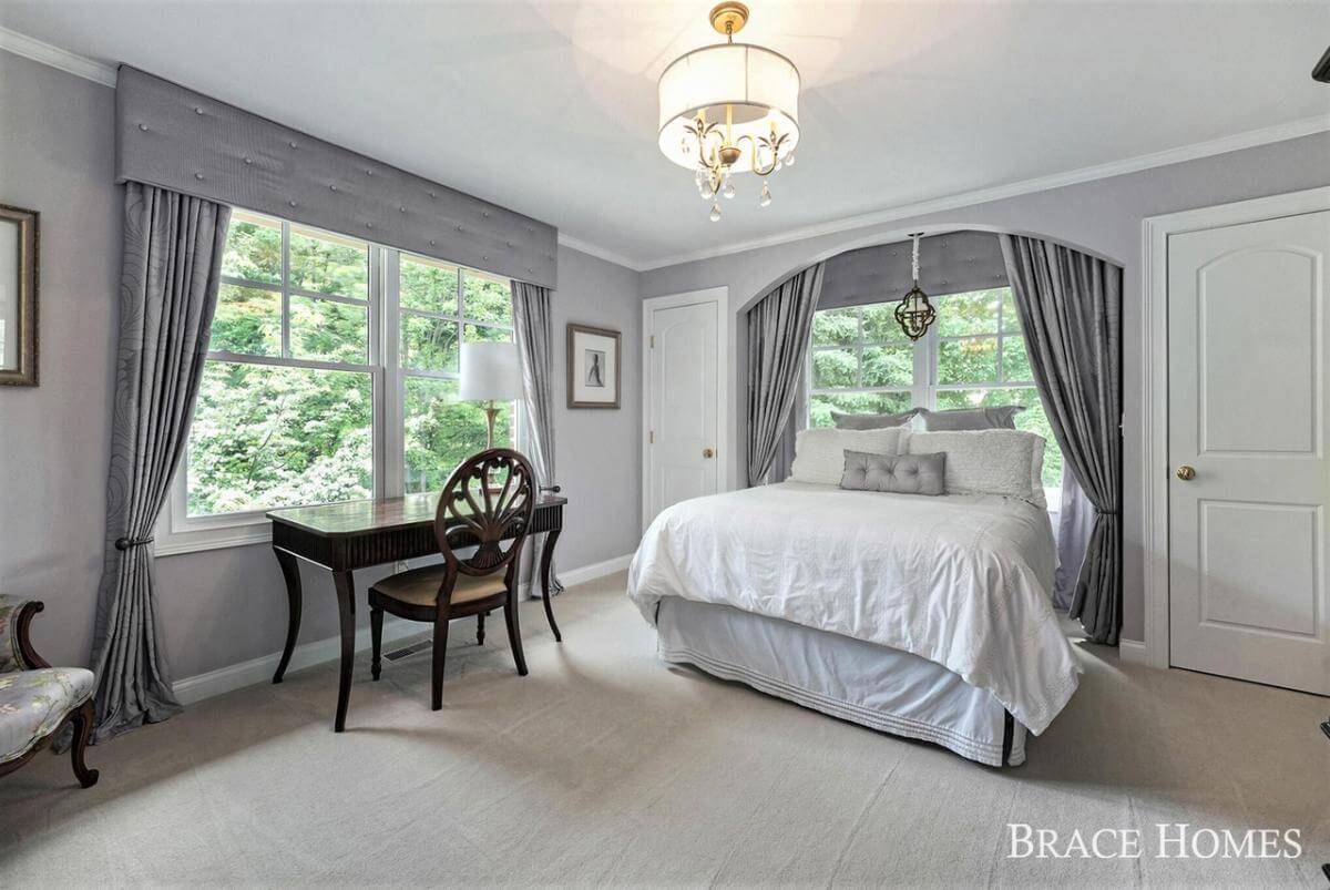 Bedroom with a skirted bed and a dark wood desk against the white-framed window.