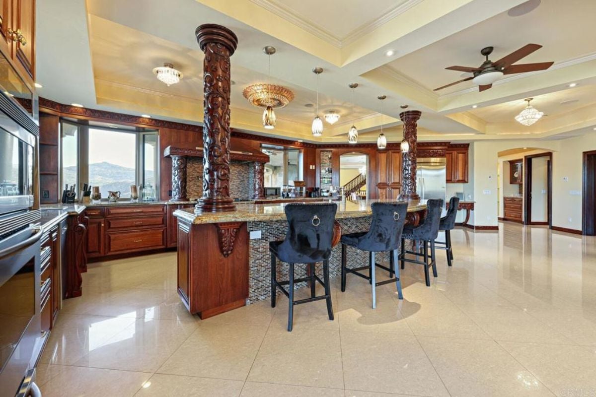 A kitchen with countertops, chairs, a ceiling fan, and cabinets.