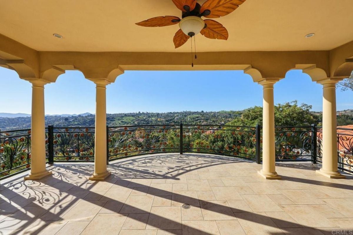 A terrace with columns, a chandelier, and a metal handrail.