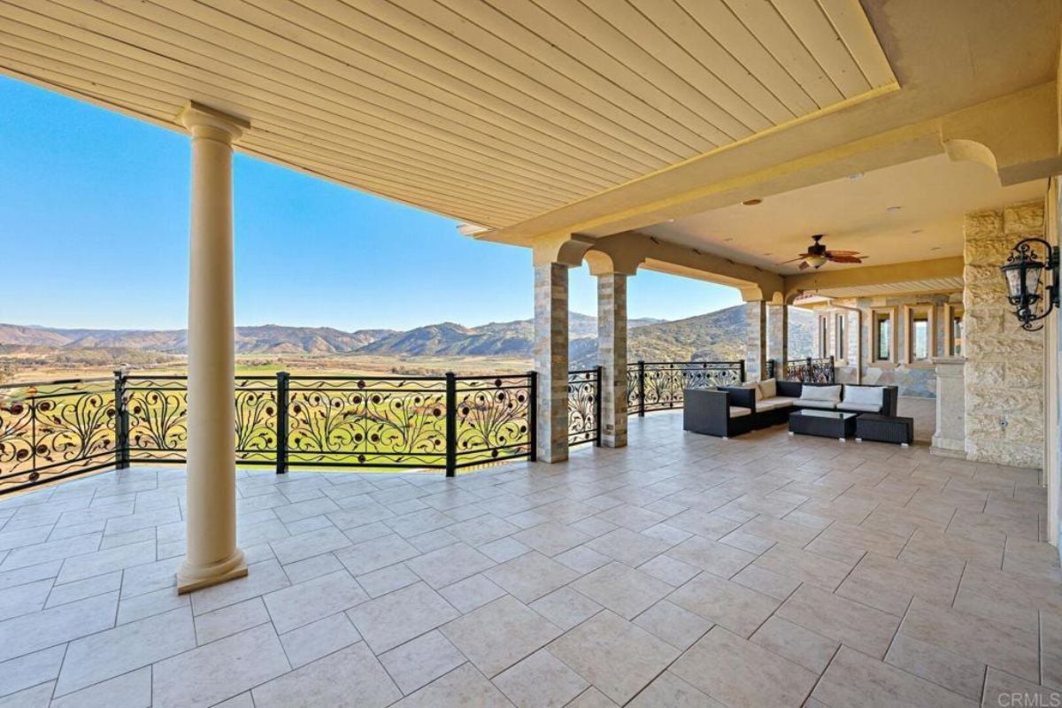 A terrace with columns, a chandelier, couch and a metal handrail.