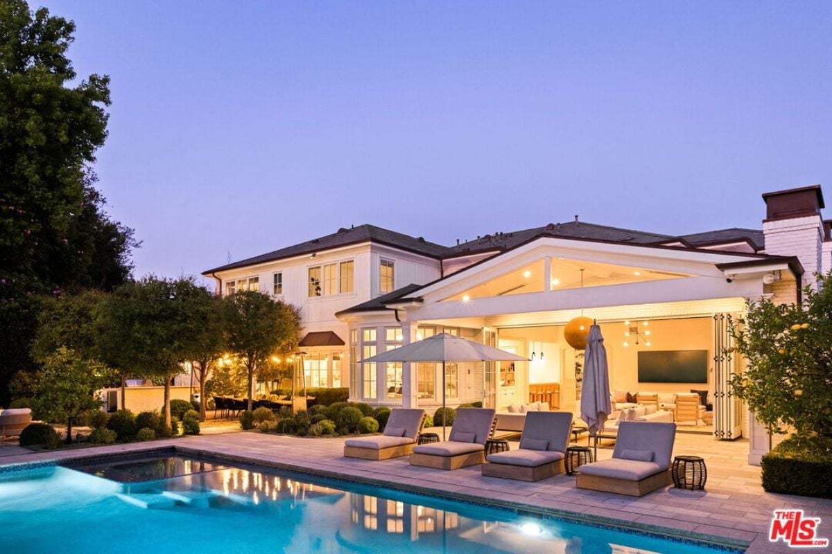 The swimming pool is surrounded by plants and trees and includes comfy chairs.