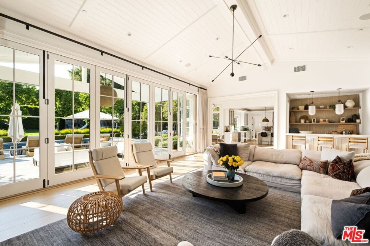 The living room features a vaulted ceiling, a rug, chairs, a couch, a round center table, and a bar.