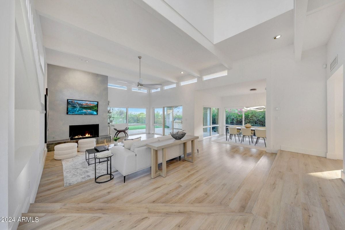 A living room with an exposed beam ceiling, TV, fireplace, chairs, and a couch.