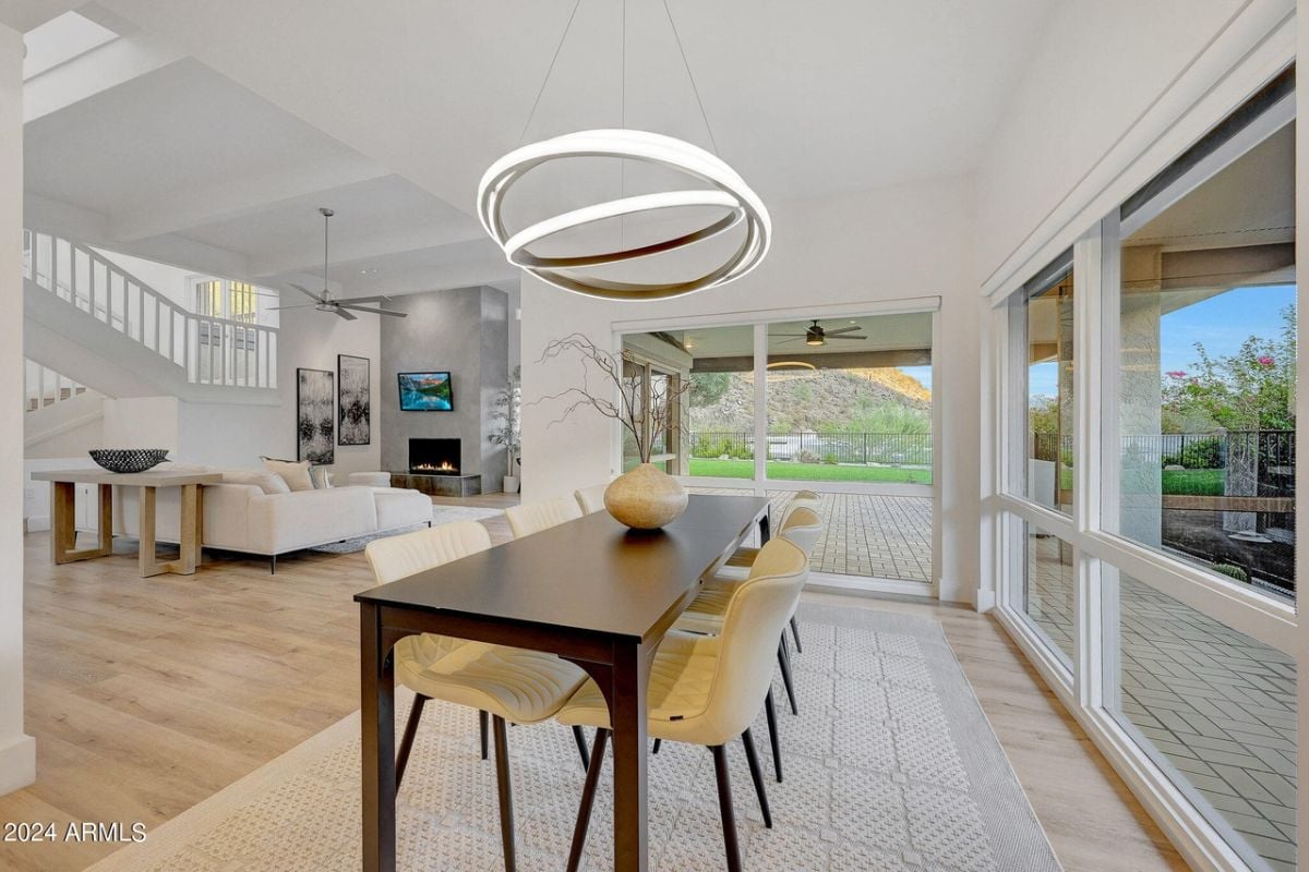 A dining room with a chandelier, windows, a rug, and a dining table surrounded by chairs.