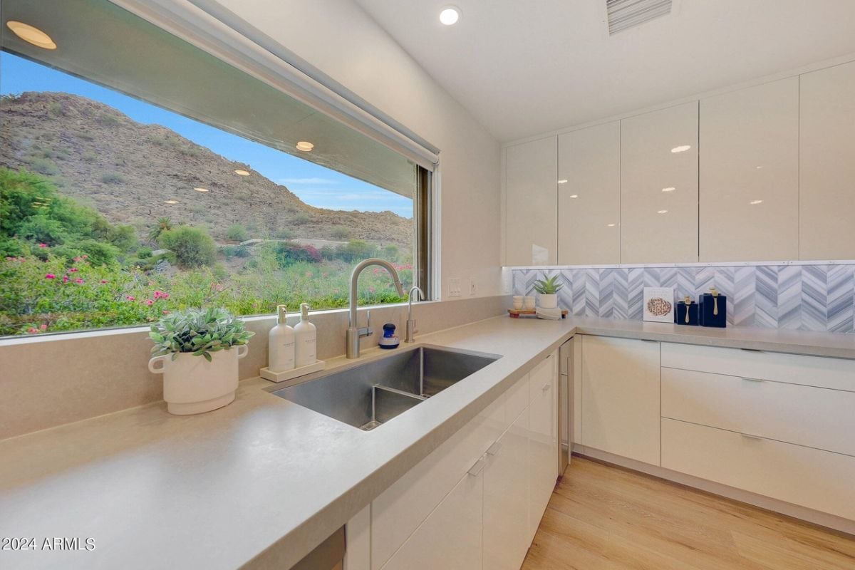 A kitchen with a window, countertops, sink, and cabinets.
