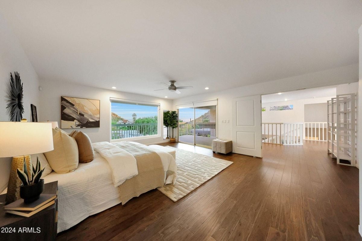 A bedroom with a bed, nightstand, rug, painting, windows, and a ceiling fan.