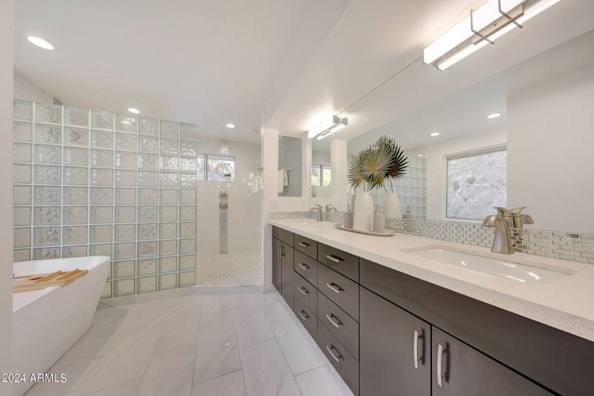 A bathroom with a dual vanity, mirror, cabinet, and bathtub.