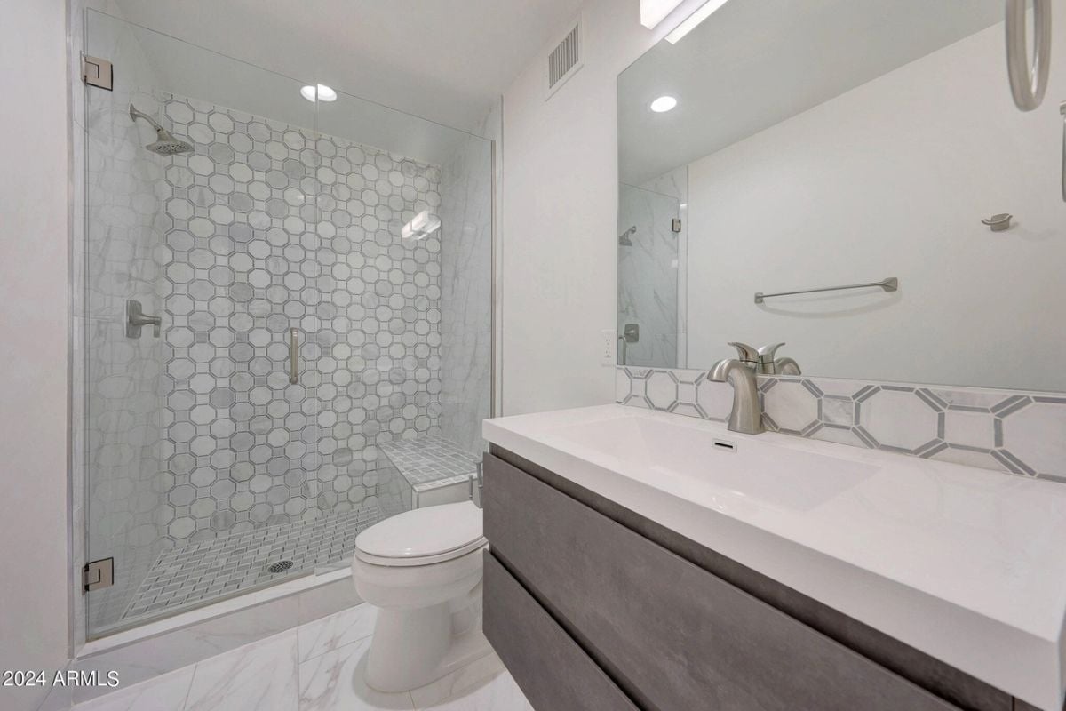 A bathroom with a vanity, mirror, toilet, and shower room.