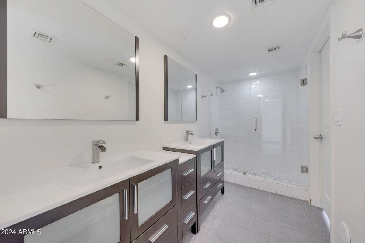A bathroom with dual vanity, mirrors, cabinets, and a shower room.
