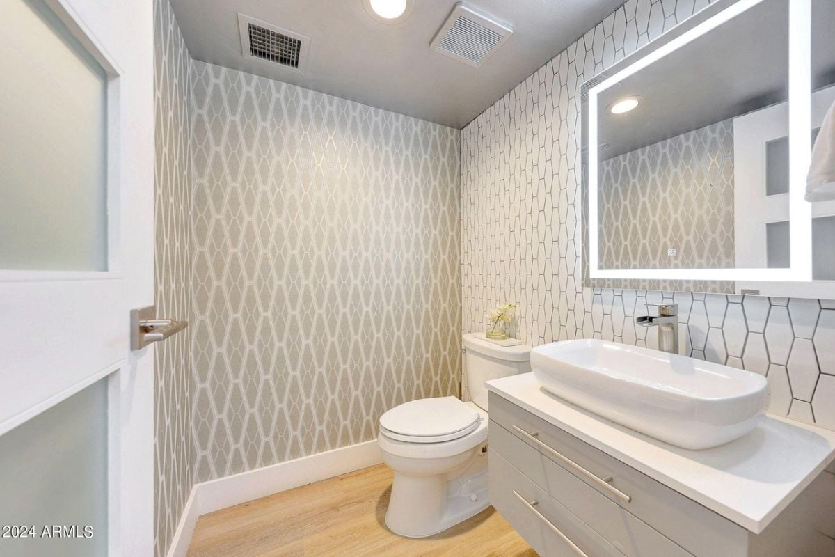 A bathroom with accent walls, a vanity, mirror, and toilet.