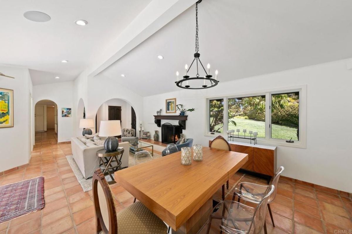 A dining area with a living space, window, and a dining table surrounded by chairs.