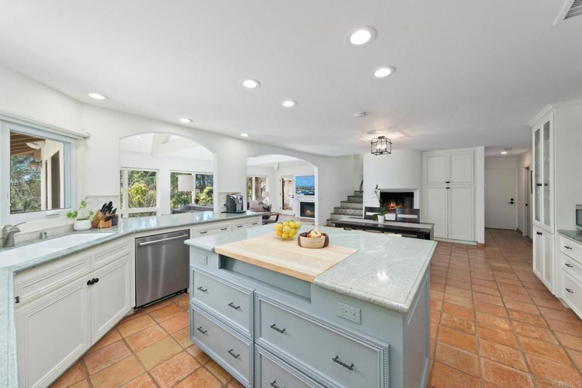 A kitchen with countertops, an island, cabinets, shelves, fireplace and a table with chairs.
