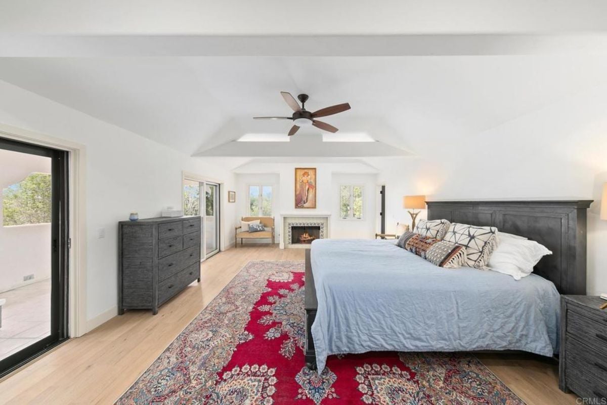 A bedroom with a bed, fireplace, rug, cabinet, ceiling fan, and rug.