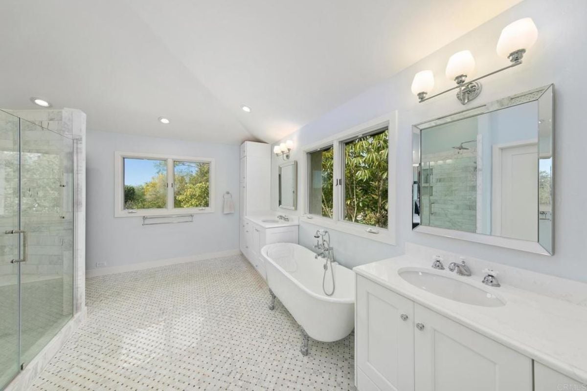 A bathroom with windows, a vanity, a mirror, a bathtub, and a shower room.