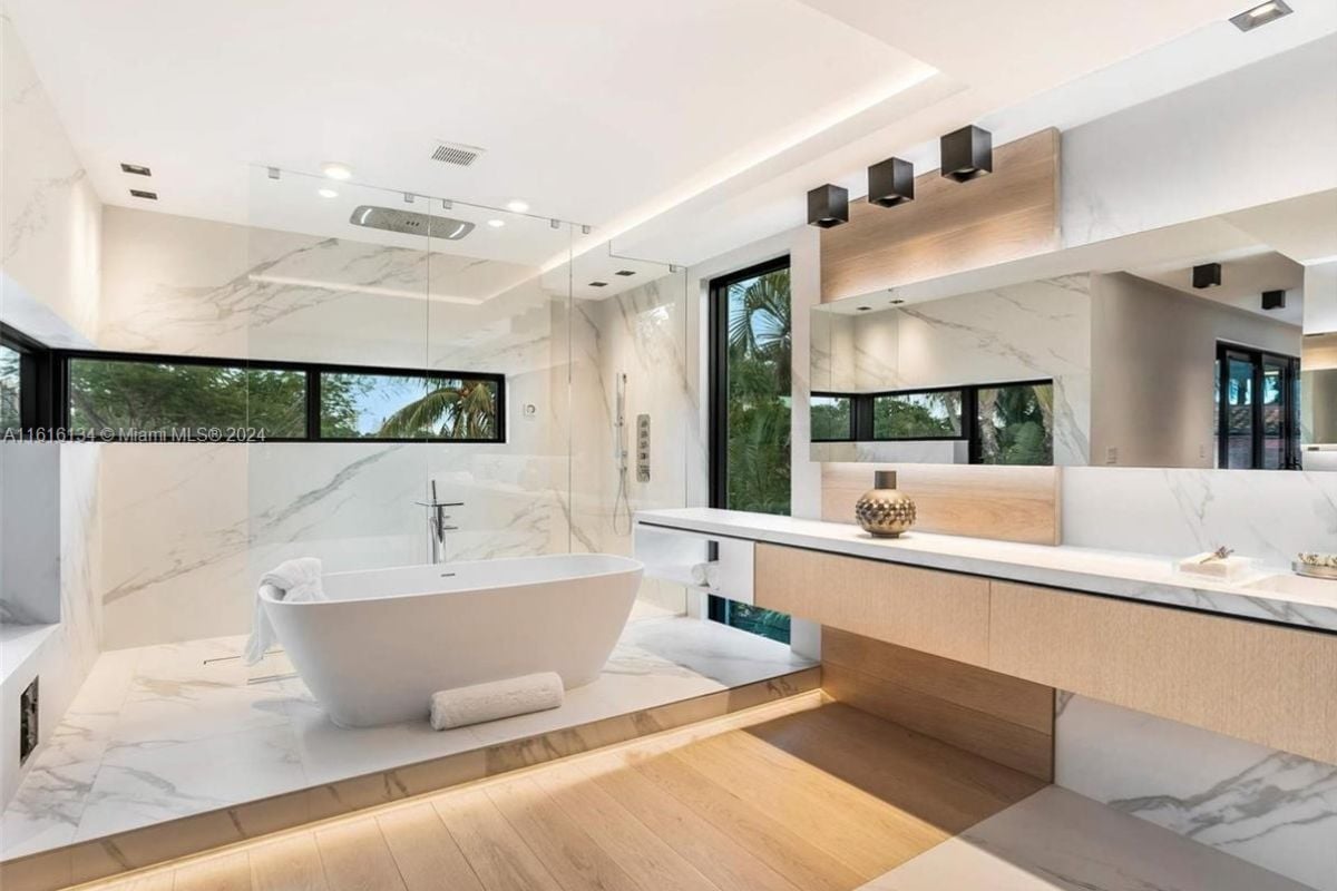 A bathroom with countertops, marble walls, a marble floor, a mirror, and a bathtub.