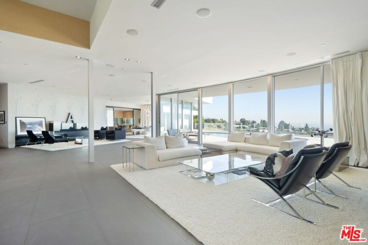 A living room with white couches, a rug, chairs, and a glass center table.