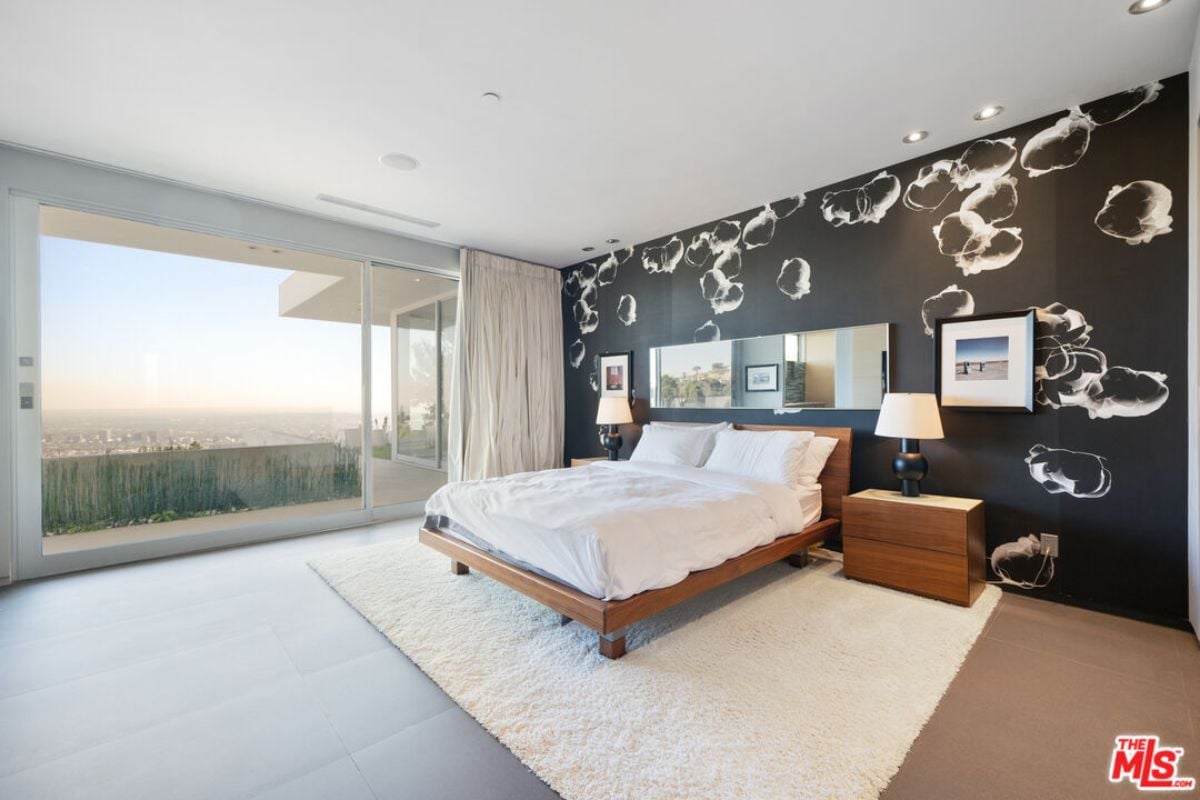 A bedroom with a bed, an accent wall, a TV, nightstands, and a rug.