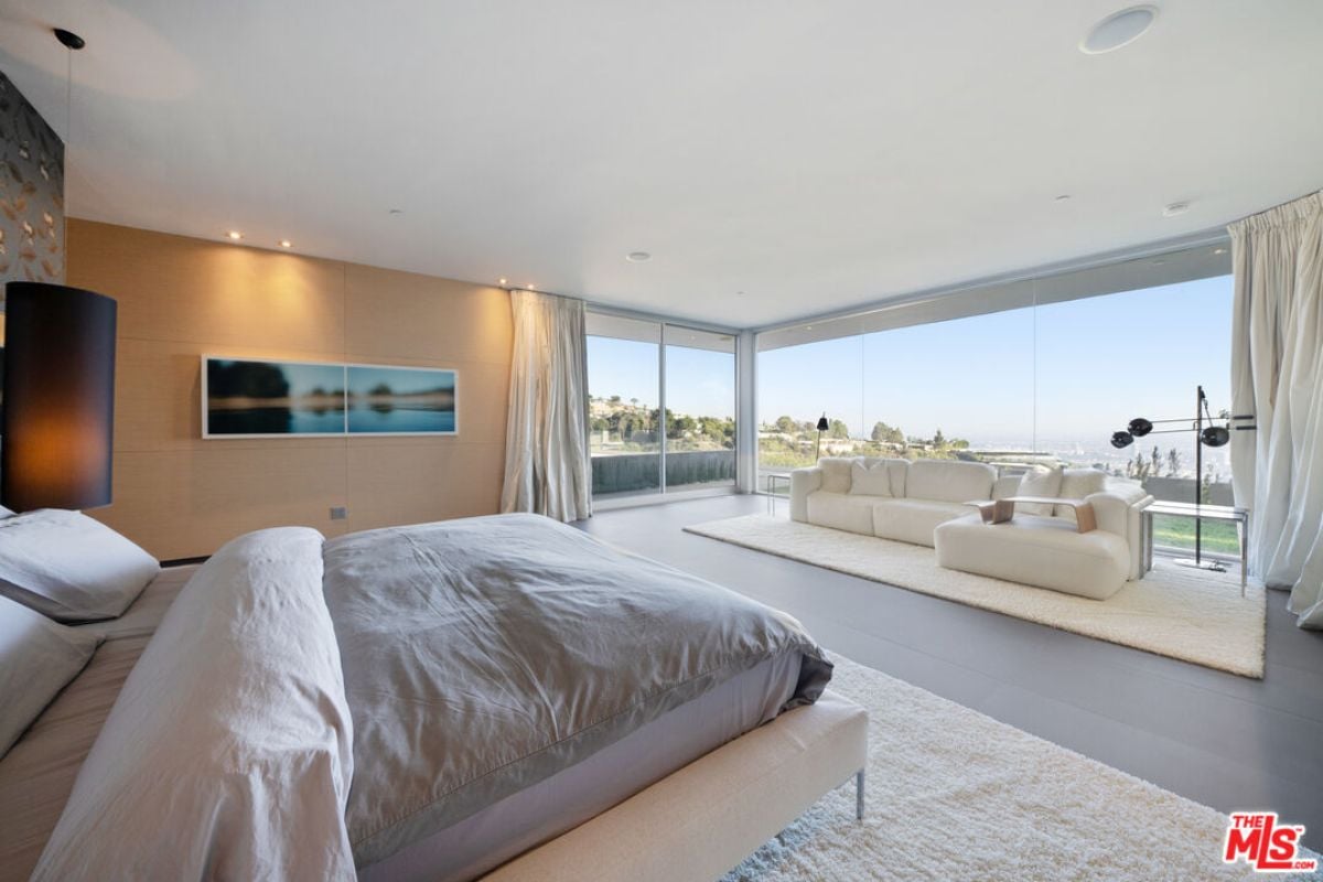 A bedroom with a bed, a rug, couches, and tall glass windows.