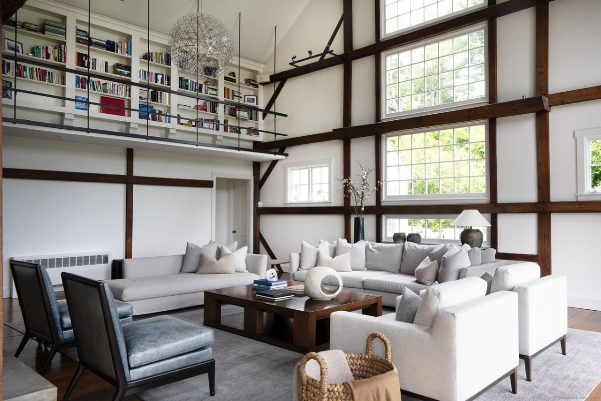 A living room with windows, white couches with pillows, chairs, and a center table.