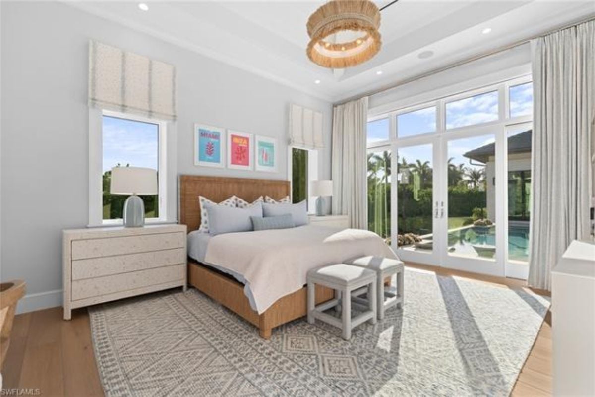 A bedroom with a bed, cabinets, windows, a chandelier, and chairs.