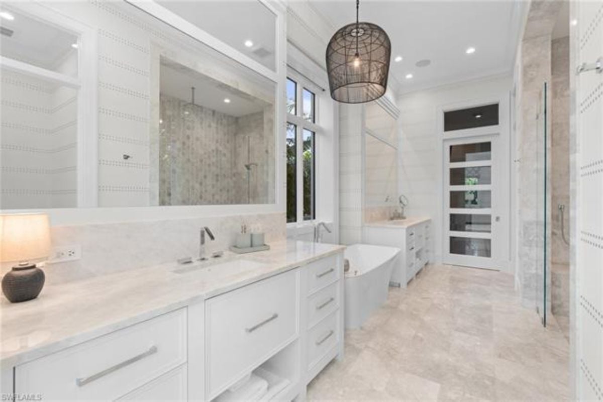 A bathroom with a tiled floor, vanities, mirrors, cabinets, and a bathtub.