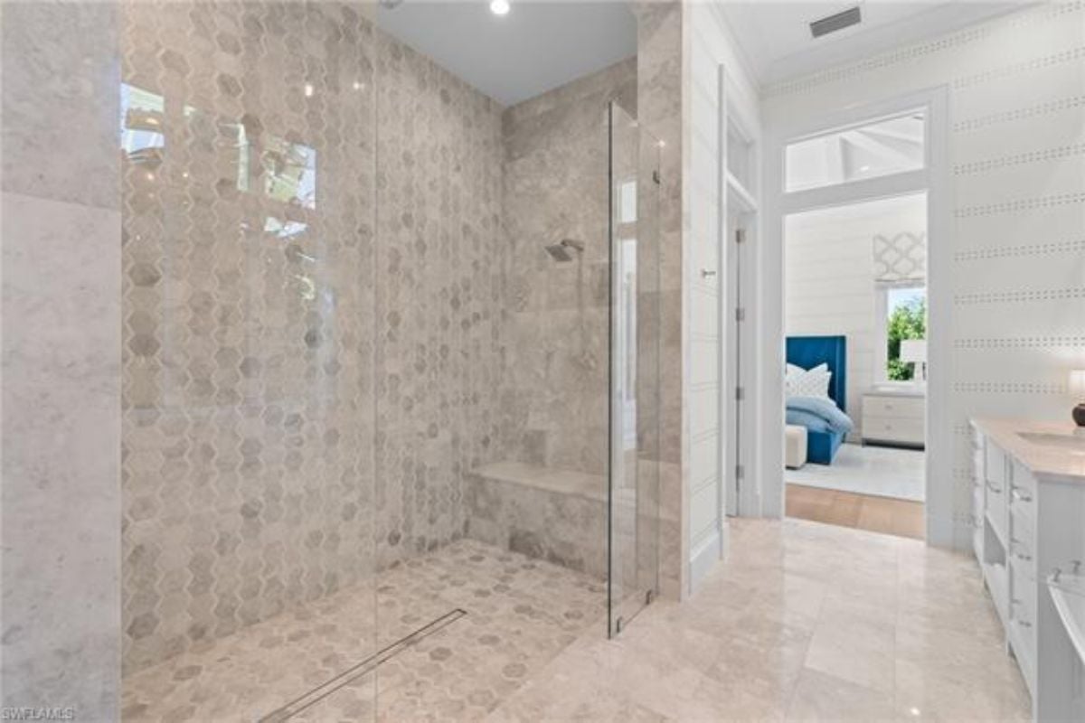 A bathroom with a vanity, cabinets, and a shower room.
