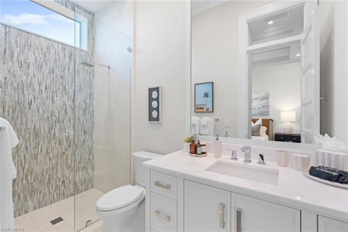 A bathroom with a vanity, cabinet, mirror, toilet, and shower room.