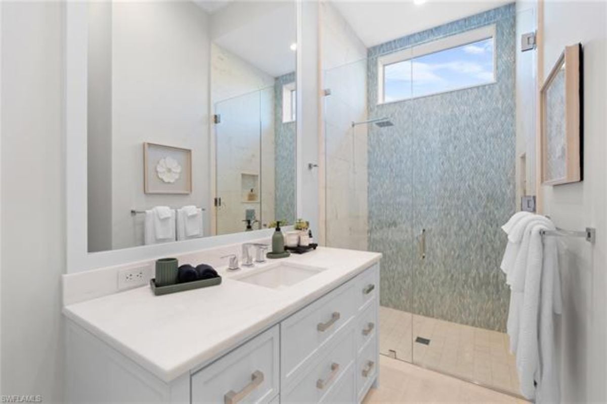 A bathroom with a vanity, cabinet, mirror, and shower room.