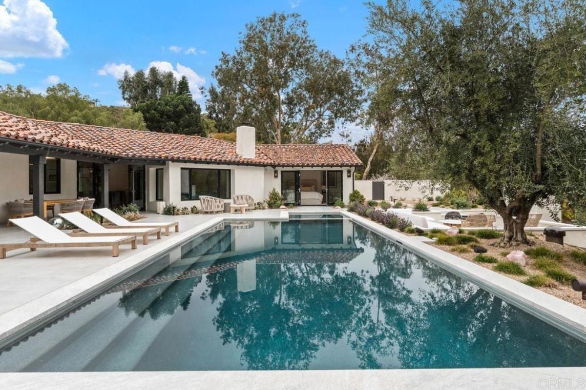 A swimming pool with comfortable chairs, bushes, and trees on the poolside.