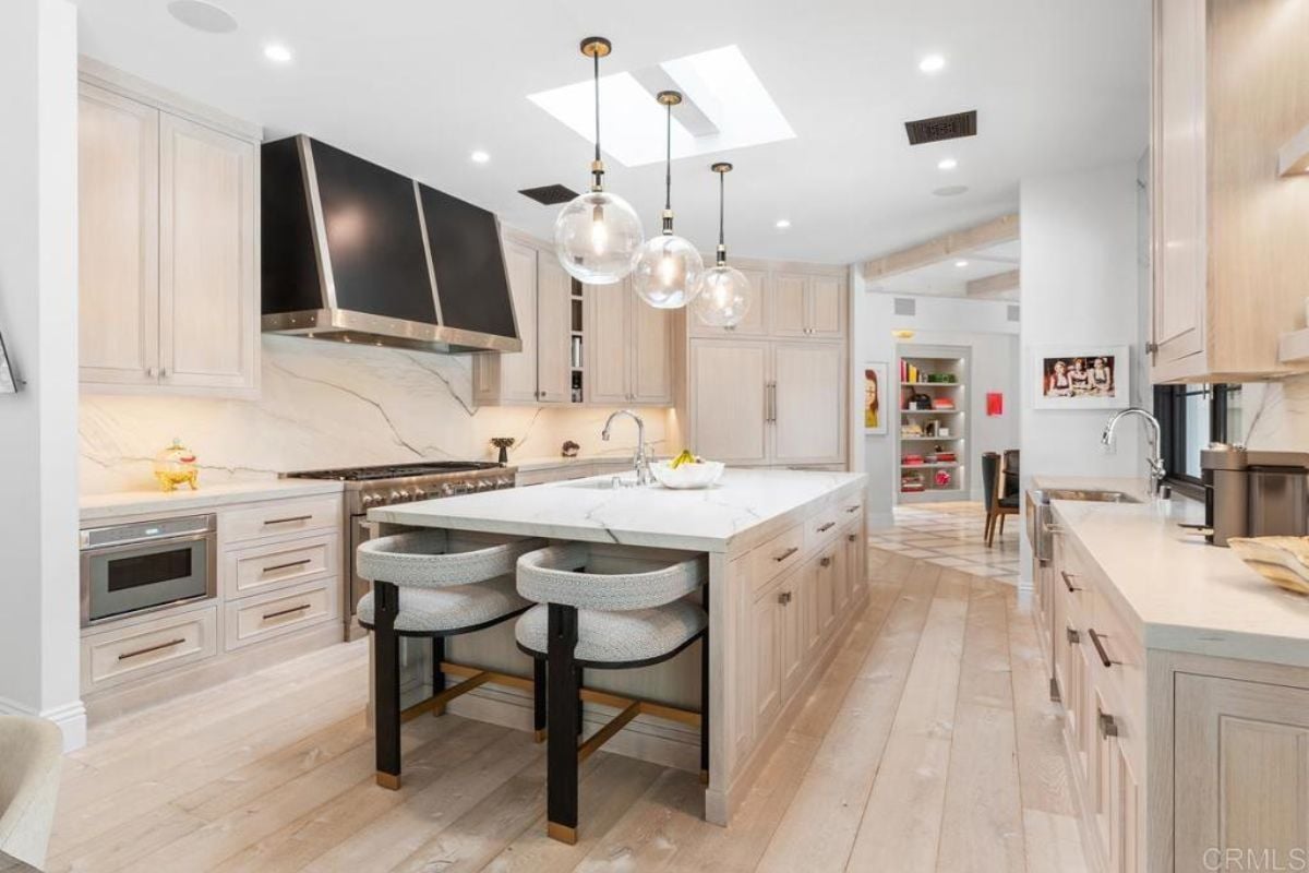 A kitchen with a center island, chairs, sink, countertops, cabinets, and kitchen appliances.