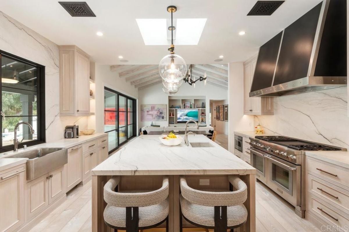 A kitchen with a center island, chairs, sink, countertops, cabinets, and kitchen appliances.