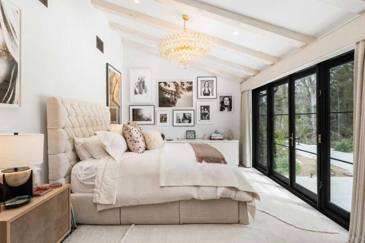 A bedroom with a bed, chandelier, cabinet, nightstand, and paintings.