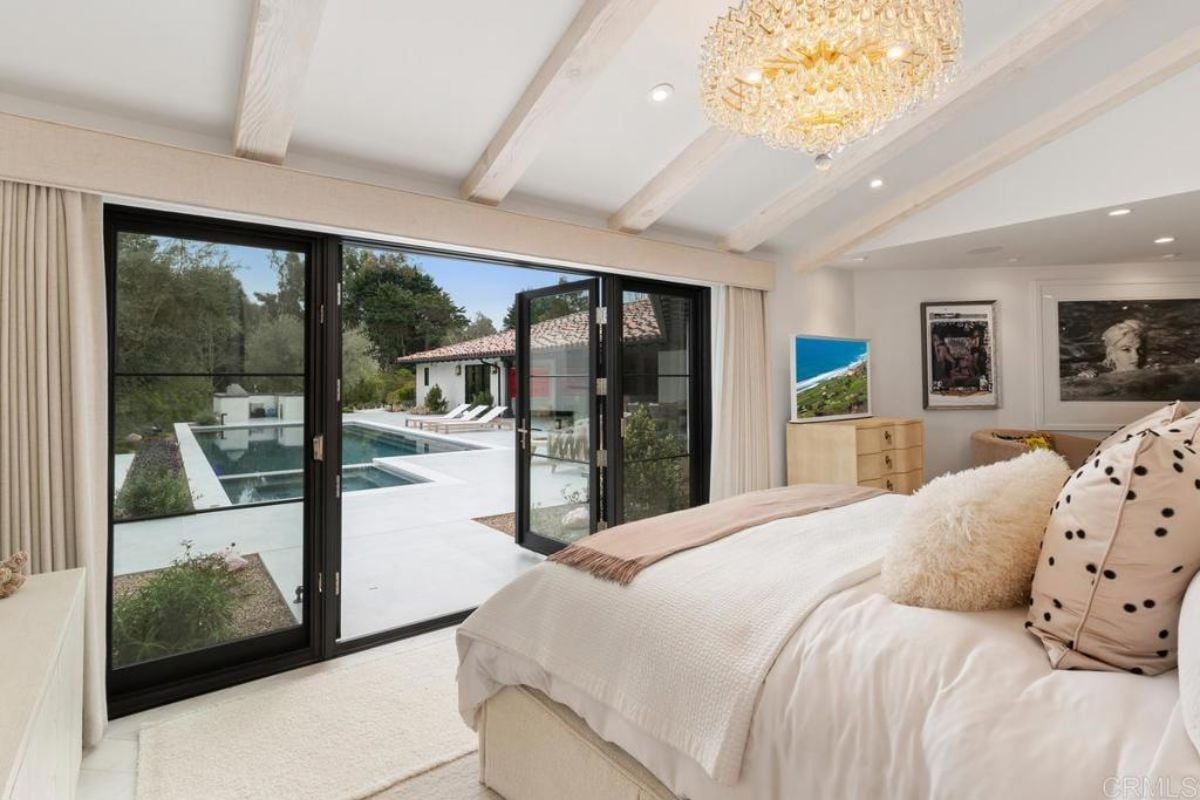 A bedroom with a bed, chandelier, cabinet, TV, and paintings.