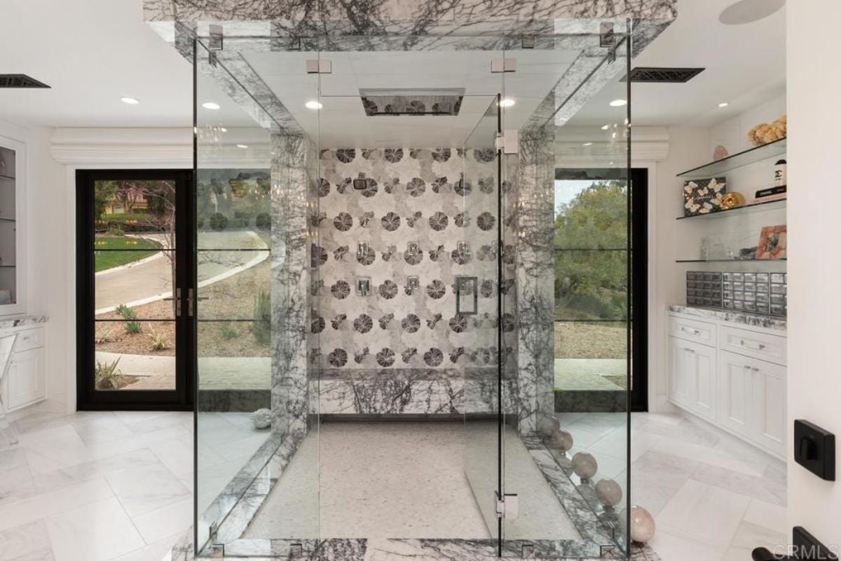 A bathroom with a tiled floor, cabinets, shelf, and glass shower room.