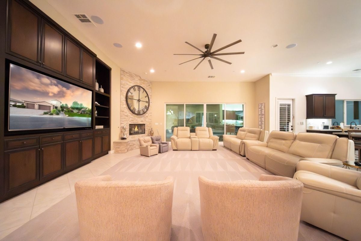 A living room with a cabinet, TV, ceiling fan, large round clock, and white couches.