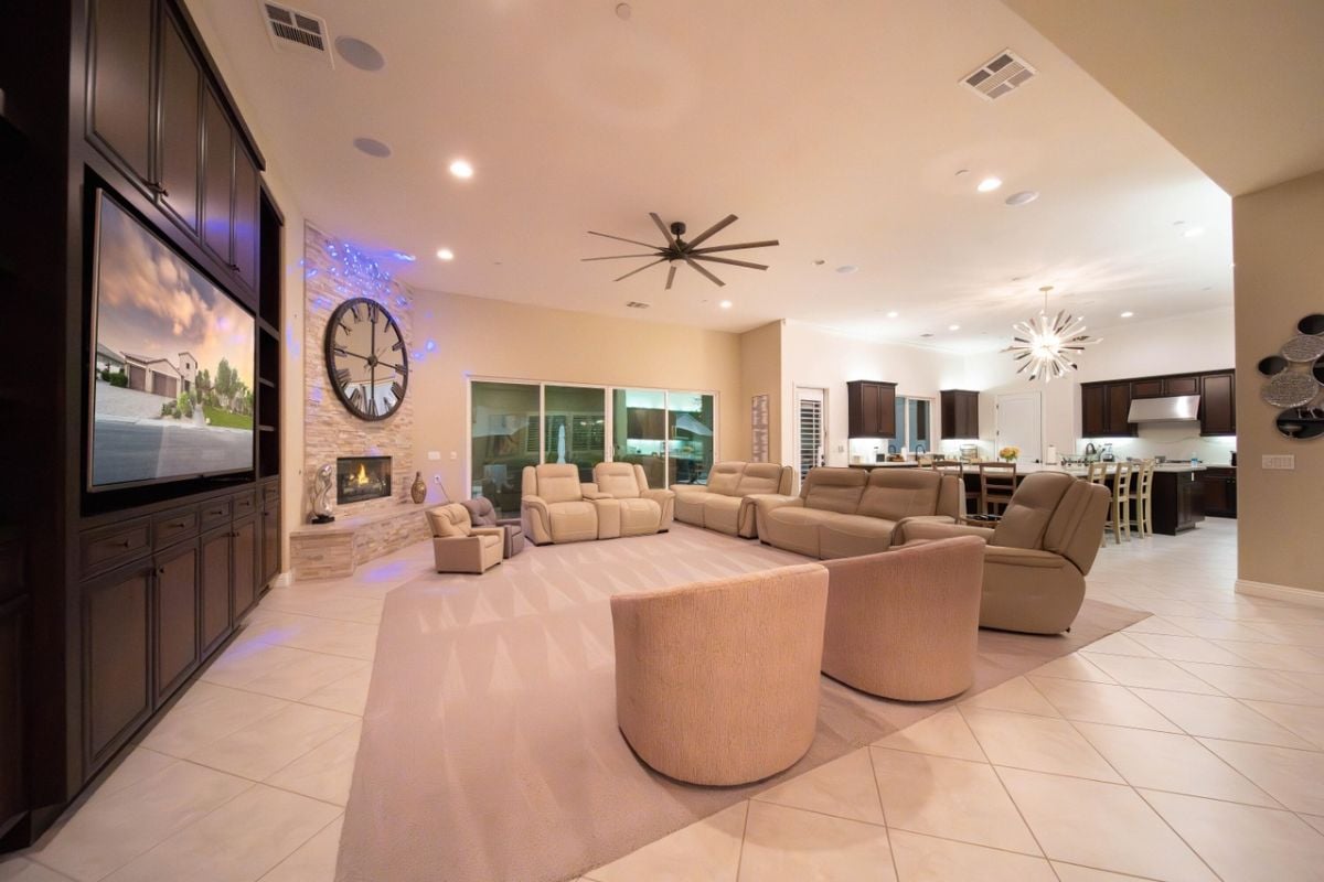A living room with a cabinet, TV, ceiling fan, large round clock, and white couches.