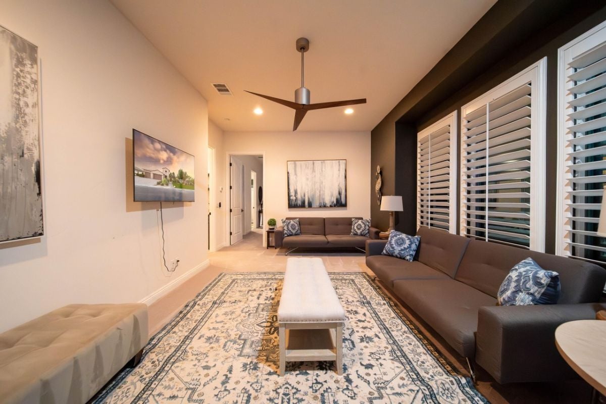 A living room with windows, couches, paintings, a rug, and a ceiling fan.