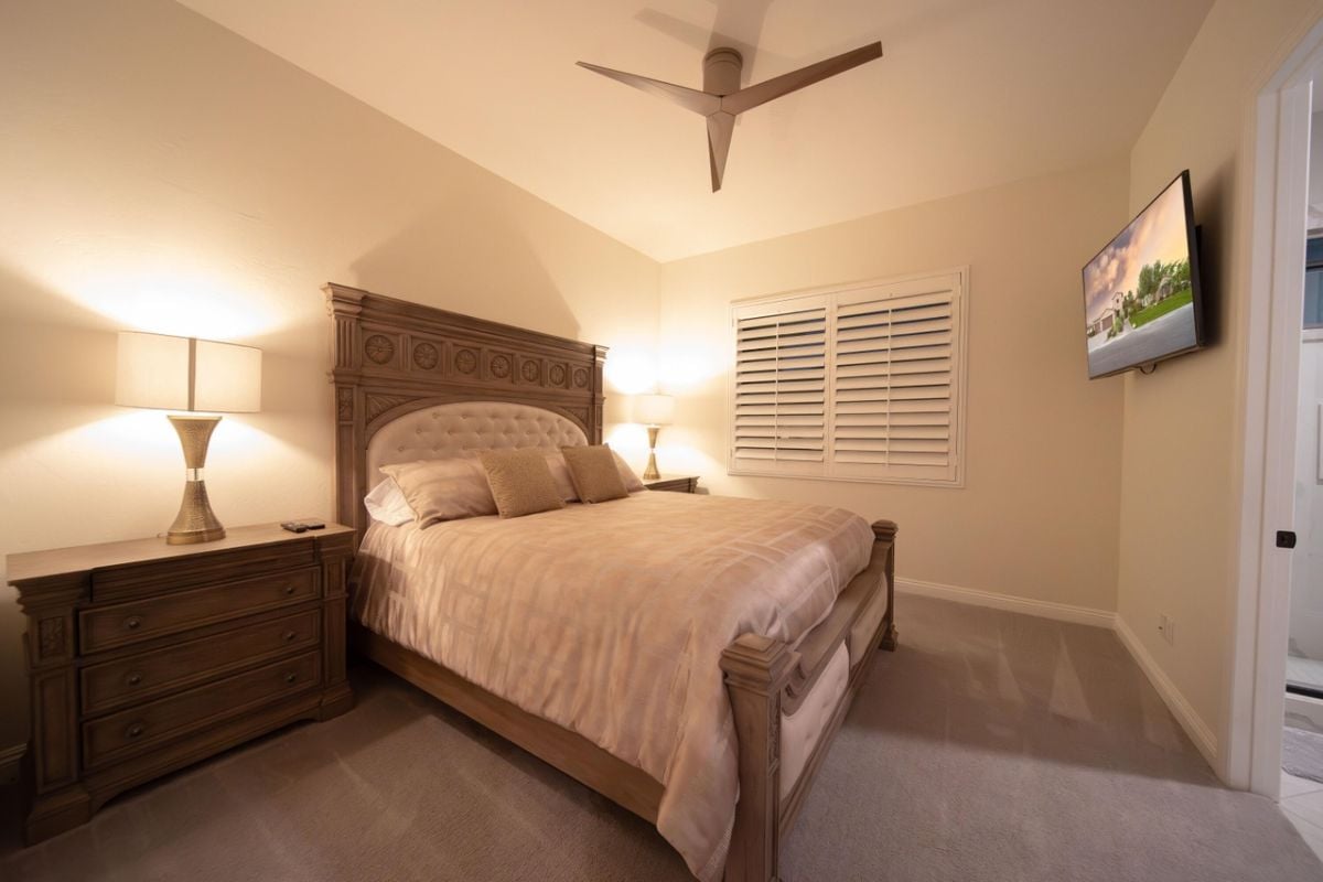 A bedroom with a bed, TV, cabinet, and ceiling fan.