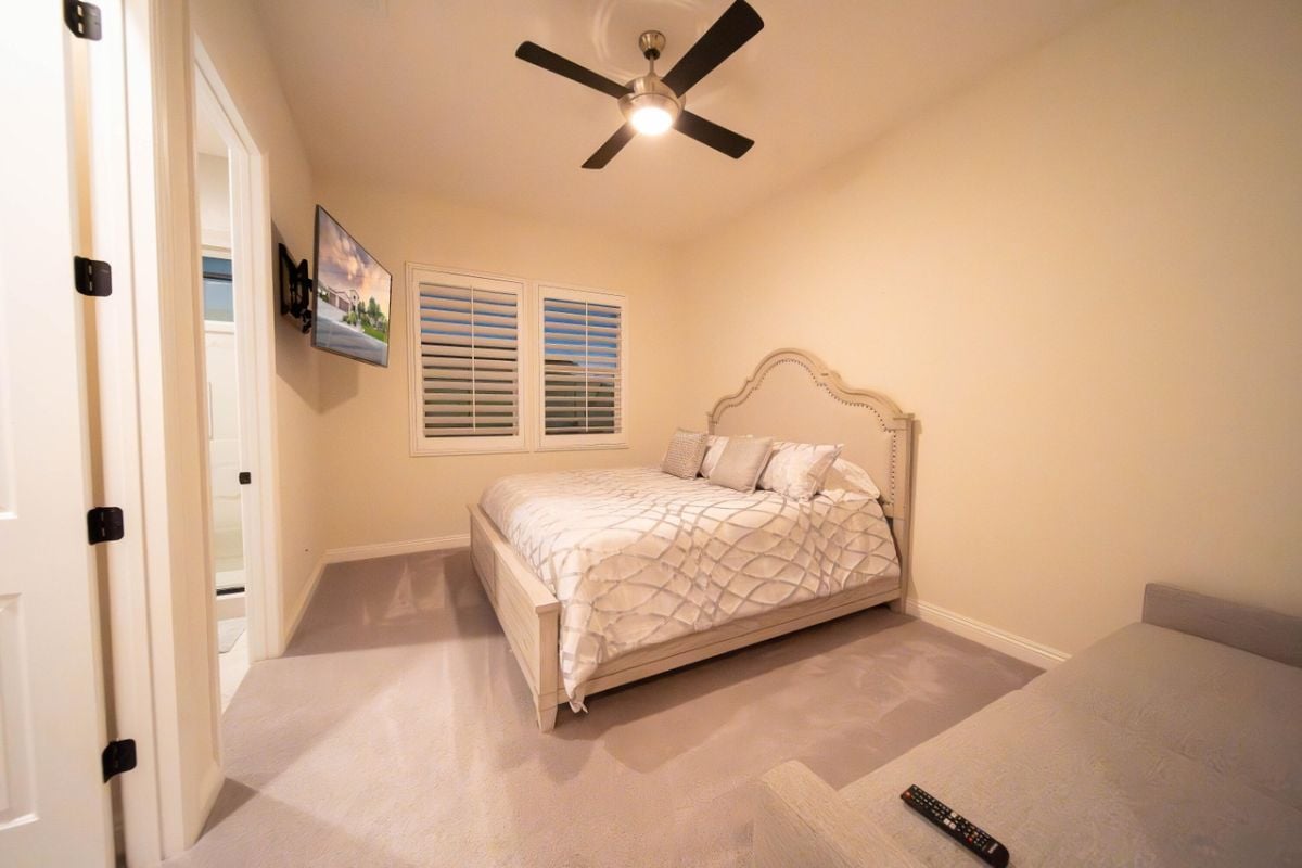 A bedroom with a bed, window, ceiling fan, and TV.